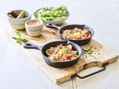 Twee gourmetpannetjes staan te sieren op een houten snijplank. Als bijgerechtjes hebben we een groene salade, opgelegde augurkjes en een cocktailsausje.