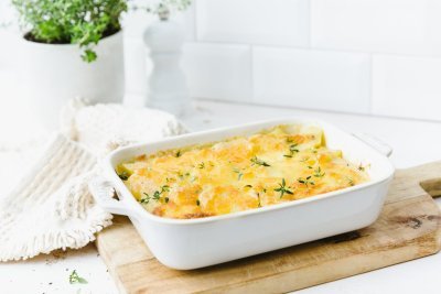 Gratin dauphinois is een klassieker die iedereen lust. Hij is klaargemaakt in een witte ovenschotel en staat op een houten snijplank op het aanrecht. Om het beeld meer sfeer mee te geven werd verse tijm, witte pepermolen en linnen doek langs de schaal gepresenteerd.