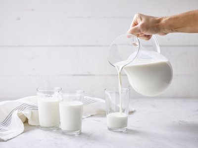 2 glazen zijn al gevuld met melk. Glazen kan met melk vult nog een glas. Glazen melk staan op marmere keukenaanrecht met linnen handdoek.