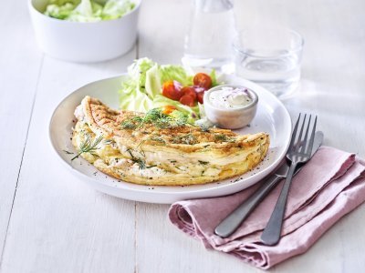 Een heerlijke omelet ligt op een wit bord. Het is een luchtige omelette die we combineren met verse kruiden en kaas. We voegde ook nog wat sla en tomaatjes toe aan het bord voor een extra portie kleur en groenten. 