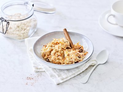 Een heerlijk ontbijtje dat smaakt naar worteltaart, dat kan je niet weerstaan! De overnight oats is geserveerd in een licht grijs diep bord, witte lepel langs en een kop verse koffie. Helemaal klaar om wakker te worden. 