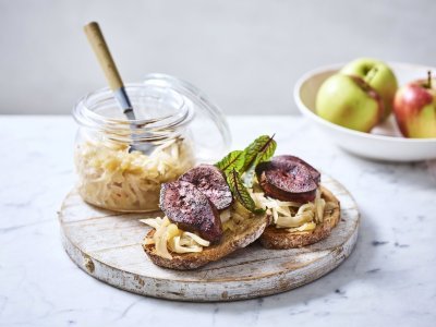 Twee toasten liggen op een houten serveerplank. Ze zijn belegt met chutney en gebakken niertjes. De overige chutney staat er langs in een glazen bokaal. 