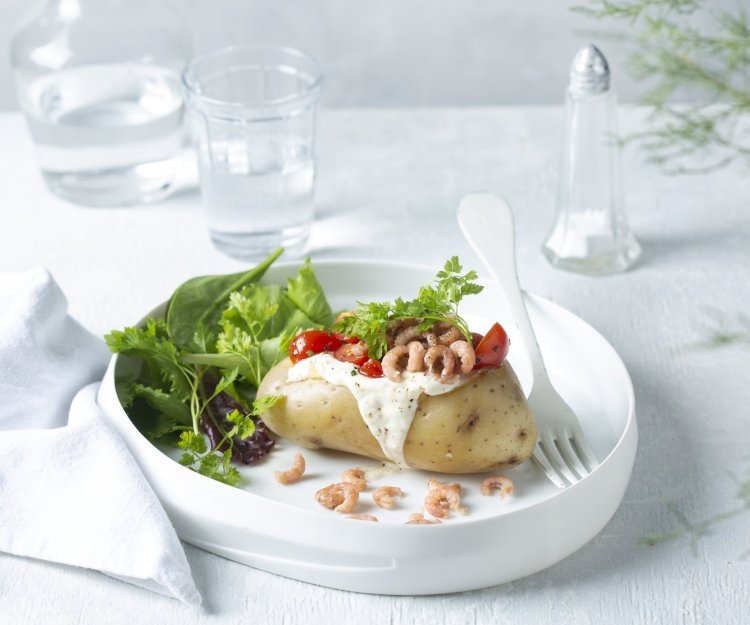 Een gepofte aardappel feestelijk afgewerkt met zure room, garnaaltjes en kerstomaatjes. Het gerechtje is afgewerkt met een groene salade dat instant kleur geeft aan het gerecht. 