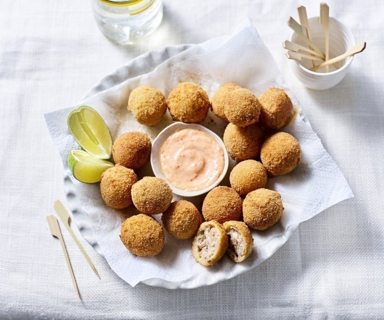 Bitterballen liggen te schitteren op een groot bord. In het midden staat een schaaltje met de pikante dipsaus en enkele partjes limoen. 