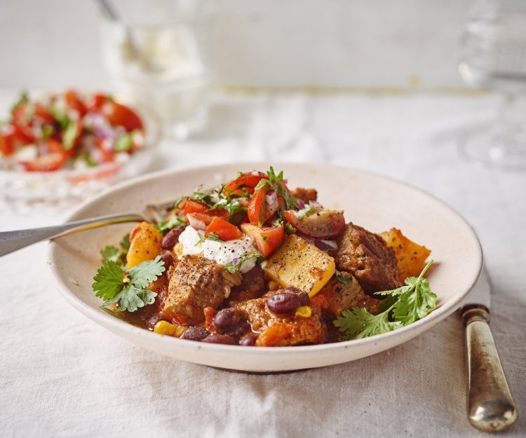 Stoofvlees gemaakt met de smaken van een chili con carne, heerlijk! Er is een portie uitgeschept in een diep bord en staat op een gedekte tafel. In de achtergrond staat de tomatensalsa en zure room om het gerechtje helemaal af te werken.