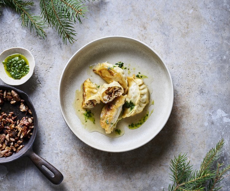 Dumplings liggen op een beige bordje, er werd een dumpling opengesneden. Zo krijg je een kijkje in de vulling op basis van boschampignons en gerookt spek. 