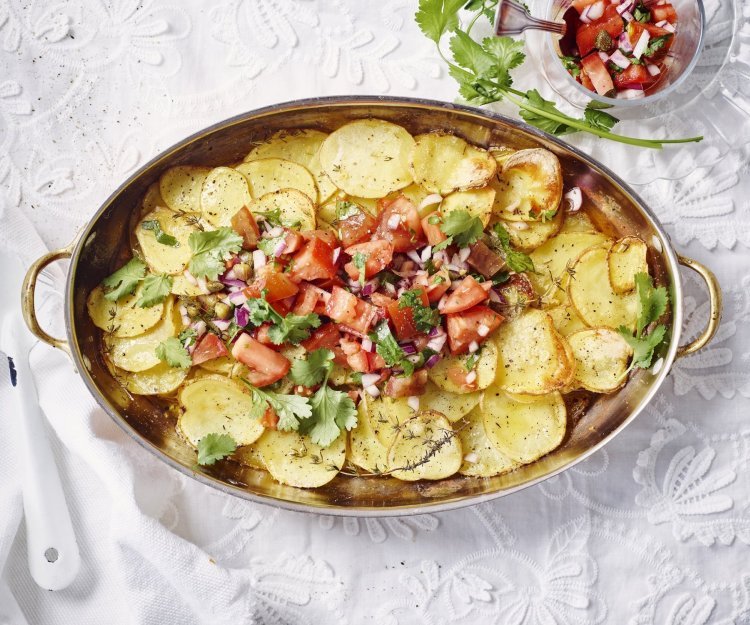 Aardappelschijfjes liggen gestapeld in een kopere ovenschaal. Hierop is de rode tomatensalsa geschept dat een mooi beeld geven tov het goudgele van de gegrilde patatjes. Her gerechtje is afgewerkt met korianderblaadjes. 