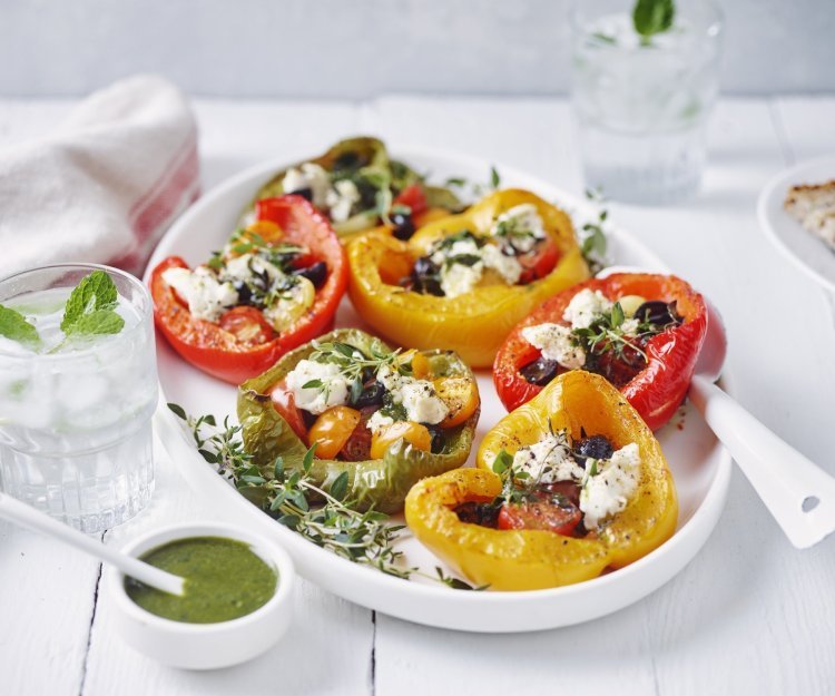 Zes halve paprika's liggen op een grote witte schaal. De paprika's zijn opgevuld met kerstomaatjes, olijven en ricottakaas. 