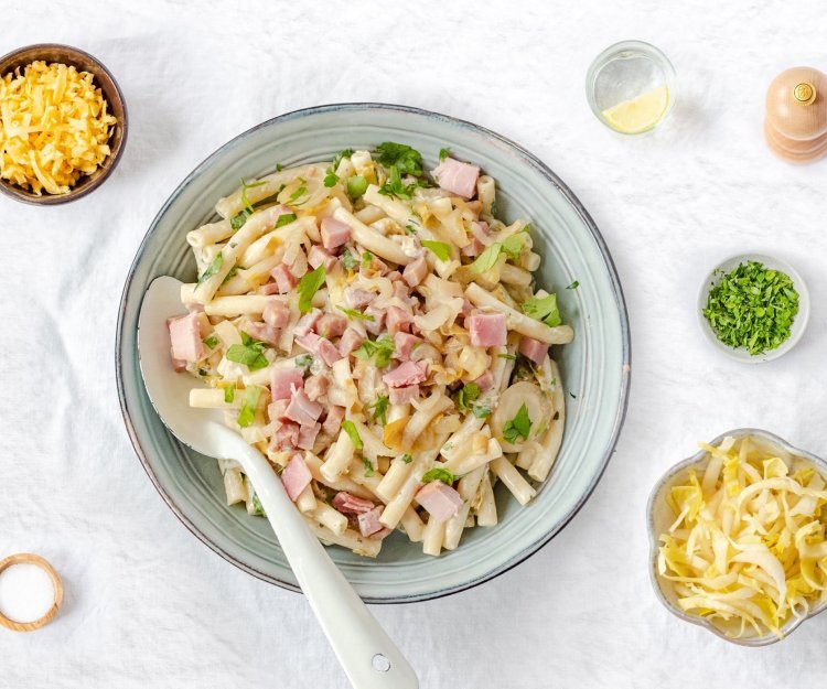 Macaroni met ham, roomkaas en witloof geserveerd in een diep bord. 