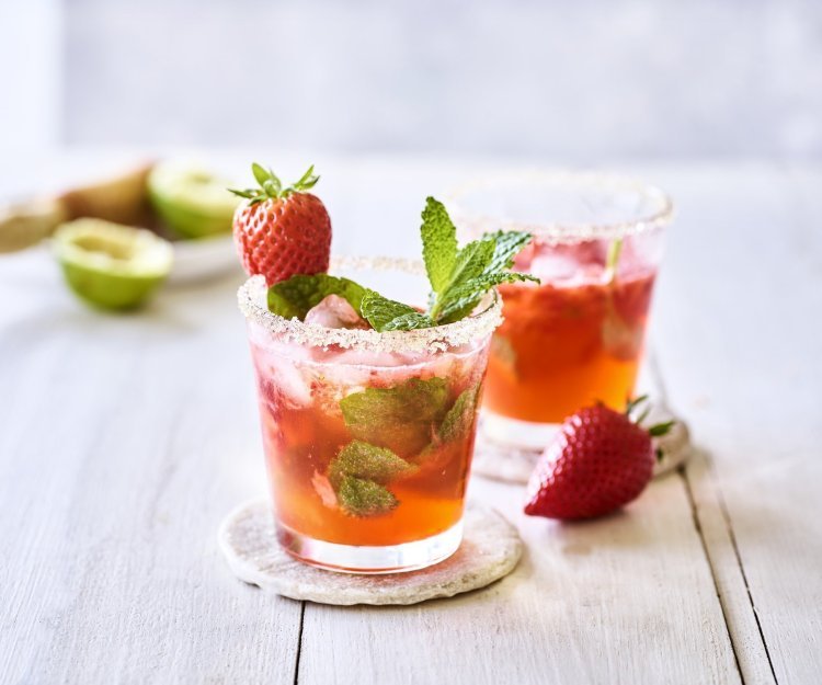 Twee roodgekleurde mojito's op de tafel, afgewerkt met verse munt en nog een aardbei. Alleen al kijken is een feestje, tijd om die cocktail te benuttigen. Het glad kreeg zelfs een suikerrandje. 