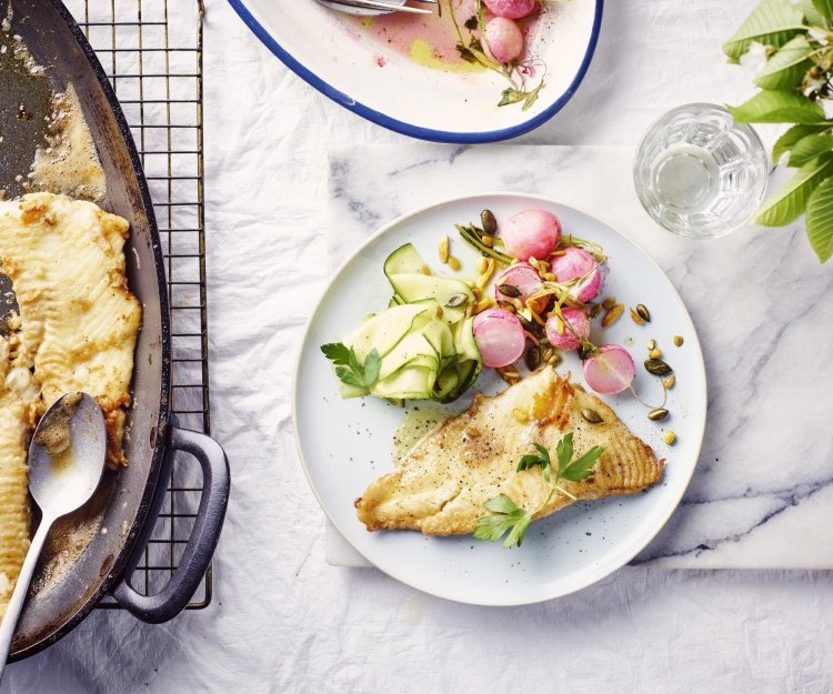 Een rond bord is gevuld met het gerechtje. De grote ovenschaal staat op tafel met al een portie uitgeschept. De radijsjes zitten in een ander ovenschaaltje en staan eveneens op tafel. De radijsjes en courgette zorgen voor een mooie kleur in het gerechtje bij de vis.