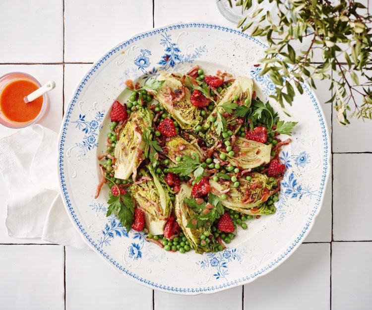 Een wit retro bordje staat op het aanrecht. Het is gevuld met een salade, gebakken spekjes en little gem. De frambozendressing is helder en roze, deze staat naast het bord in een glazen potje. 