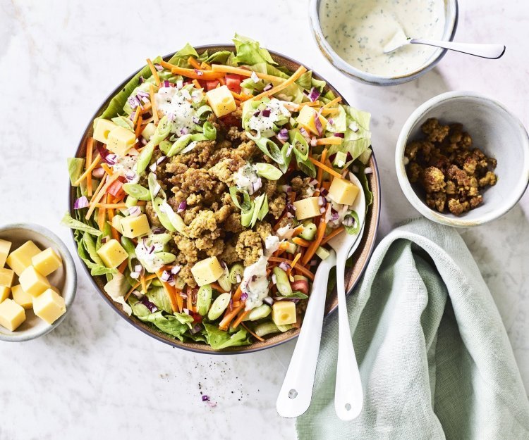 Een grote salade kom staat op het aanrecht, hij is gevuld met gemengde sla, komkommer, tomaten, worteltjes, stukjes kaas en gebakken gehakt. We werkte de salade af met een ranchdressing op basis van zure room en verse kruiden.