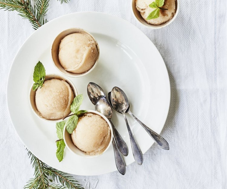 Drie sorbets staan op een wit rond bord, afgewerkt met een muntblaadje. De koffielepeltjes liggen ook op het witte bord, de tafel is aangekleed met takjes kerstboom.