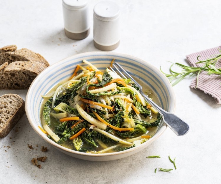 Op de tafel staat een portie uitgeschept van het vegetarische stoofpotje boordevol groenten. Denk maar aan witloof, savooikool, pastinaak en wortel. Wij serveren dit gerechtje met enkele sneetjes zuurdesembrood. 