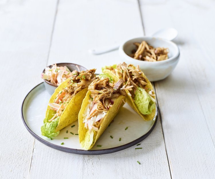 Krokante taco's liggen op een bordje, ze zijn gevuld met stukjes varkensvlees en een slaatje van kool. 