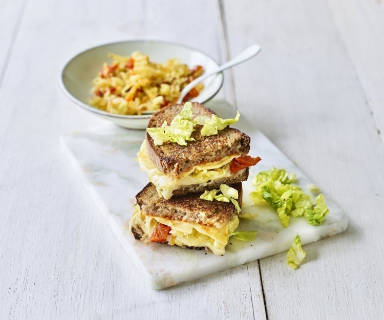 Een heerlijke cheesy toast ligt op een marmere snijplank. De toast is gevuld met 2 Belgische kazen, kimchi en chilisaus. 