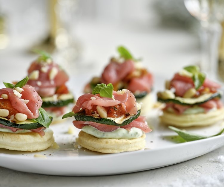 Feestelijke hapjes die de show stelen! Deze torentjes van kruimeldeeg, carpaccio en Belgische ricotta is een schot in de roos voor tijdens de feestdagen. Onderaan ligt een koekje van kruimeldeeg, hierop de ricotta met basilicum, rundvlees, gegrilde courgette en opnieuw rundvlees. Afwerken deden we met pijnboompitten en een extra blaadje basilicum.