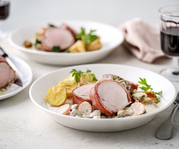 Op tafel staan twee porties uitgeschept. Het heerlijk bereide varkenshaasje ligt op de romige champignonsaus met plakjes wortel. Er liggen ook ovengeroosterde aardappeltjes bij. Langs het bord ligt een servette, glaasje rode wijn en bestek. 