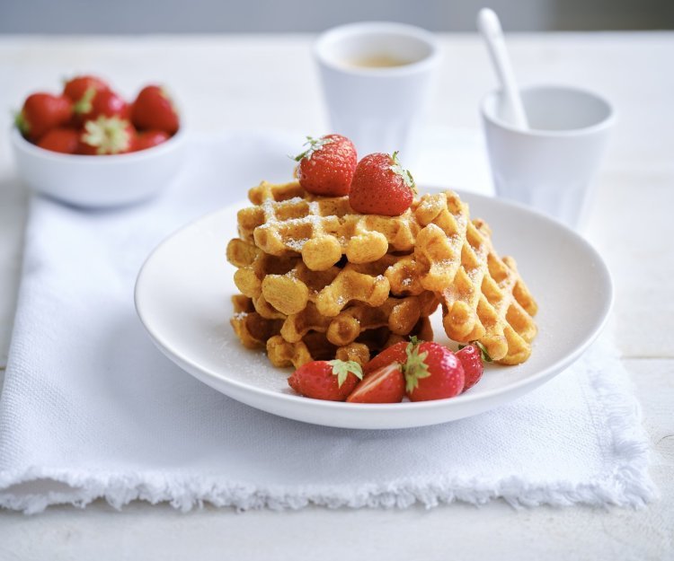 Op een bordje liggen enkele wafels met verse aardbeien en wat bloemsuiker. Er staat ook nog een tasje koffie langs. 