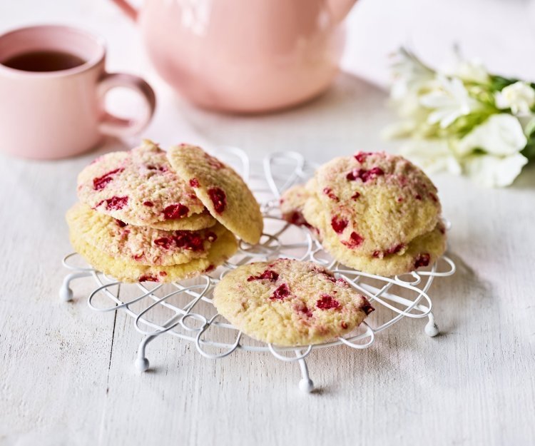 Op een kleine taartrooster liggen enkele koekjes te drogen. De koekjes hebben rode vlekjes van de framboosjes. Er staat een theepot langs met al een uitgeschonken thee in bijpassende roze tas. 