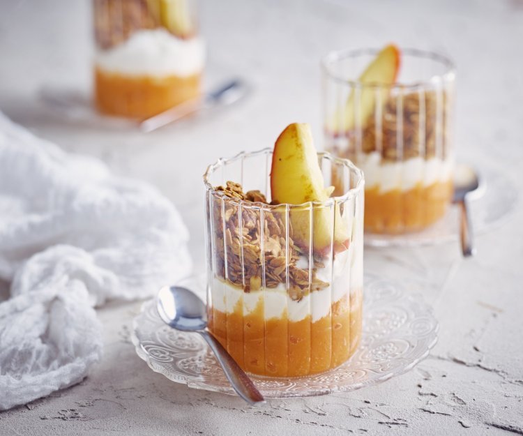 Op tafel staan 3 glaasjes gevuld met dit ontbijtje. Onderaan ligt een lepeltje zoete aardappel, hierbovenop de kwark, granola en een stukje gestoofd appel. De kleuren van dit ontbijtglaasje zijn gewoon om blij van te worden. 