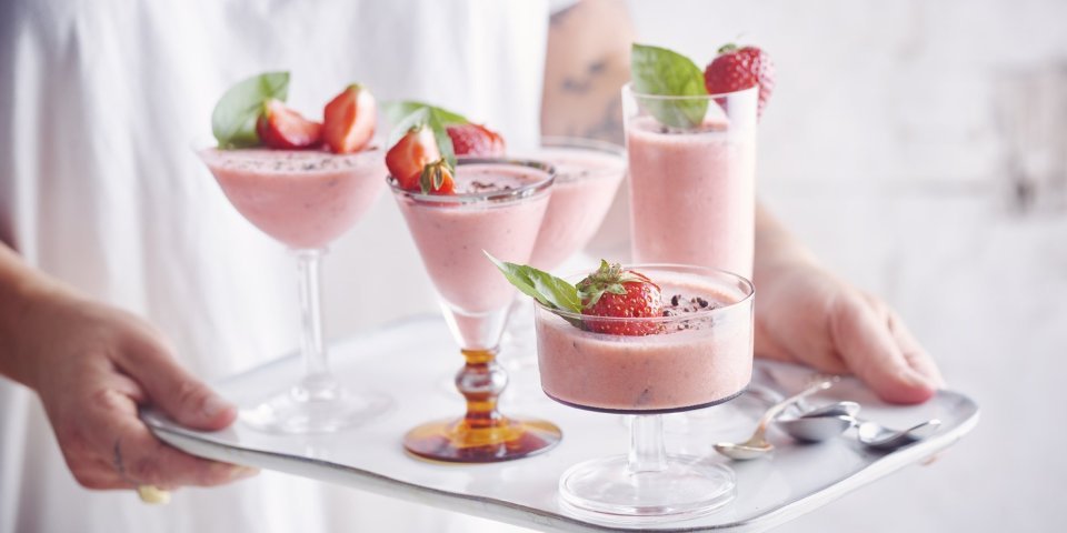 Roze bavarois geserveerd in verschillende glaasjes op een dienplateau. Een vrouw met witte t-shirt draagt deze roze dessertjes, klaar om naar de gasten te brengen.