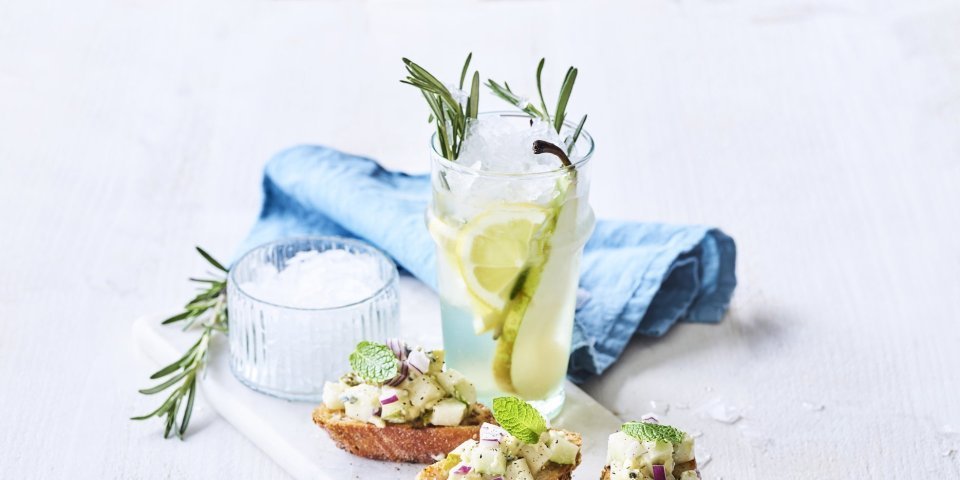 Rozemarijnlimonade met peer staat op tafel, klaar om te proeven. Wij serveren hem met burschetta met perensalsa en blauwe schimmelkaas