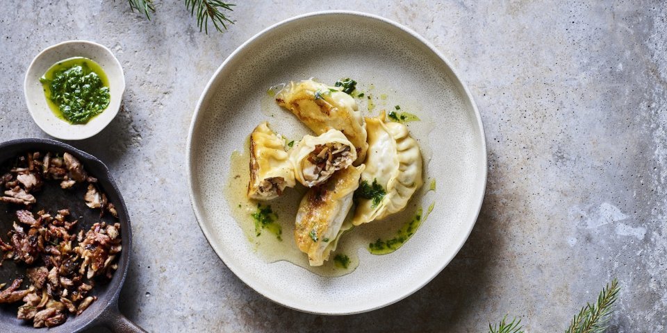 Dumplings liggen op een beige bordje, er werd een dumpling opengesneden. Zo krijg je een kijkje in de vulling op basis van boschampignons en gerookt spek. 