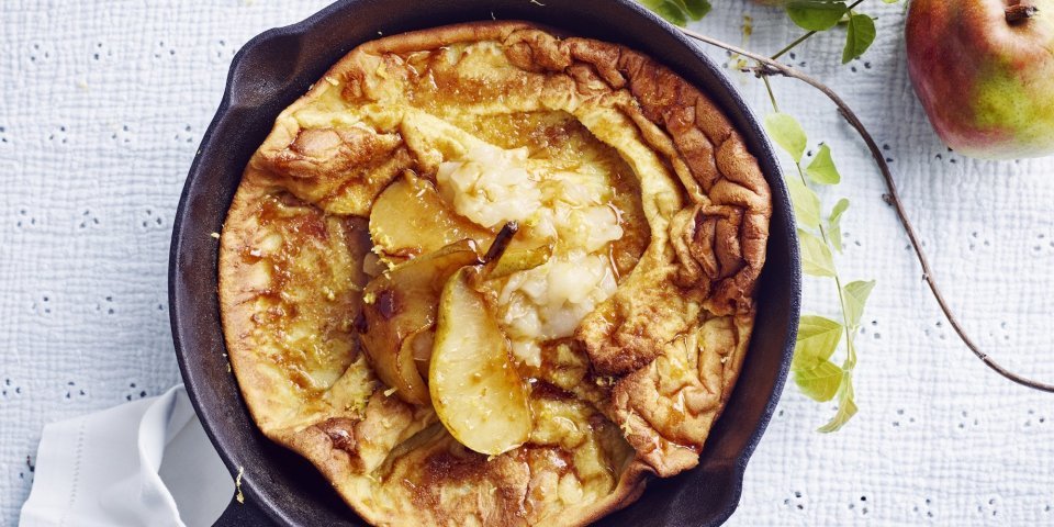 Een ovenpannenkoek met heerlijke peertjes, hij komt net uit de oven en ligt nog in de pan. Er liggen 2 verse peperen langs.