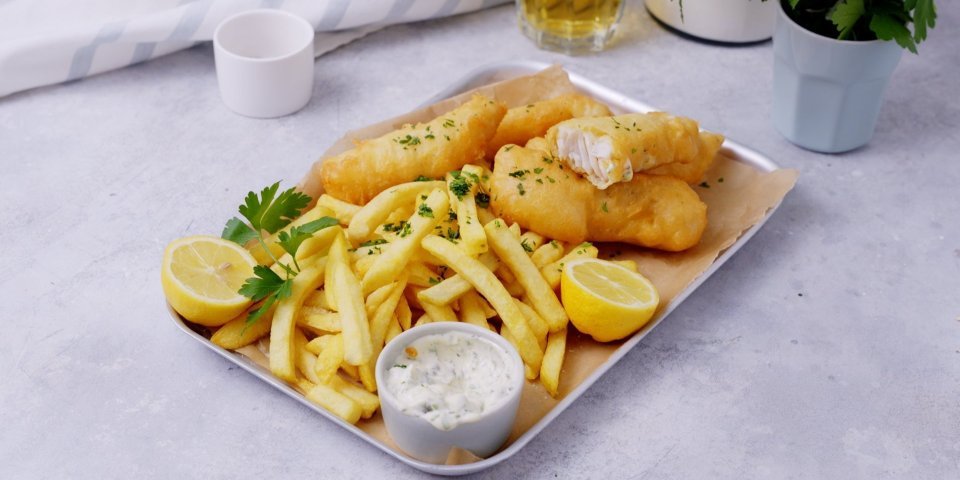 Een metalen schotel is gevuld met homemade knapperige frietjes, fishsticks en verse tartaarsaus. Het gerechtje is afgewerkt met verse gesnipperde peterselie.