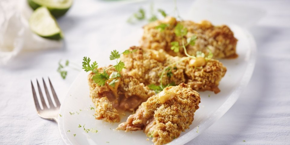 Heerlijke garnaalkroketten liggen op een ovaal wit bordje. Er liggen partjes limoen in de achtergrond en vorkje om meteen aan te vallen. 