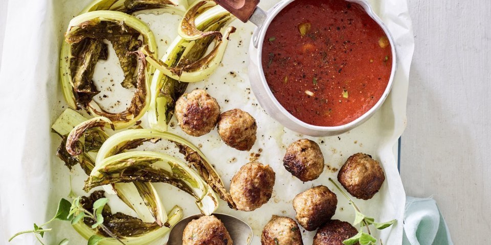 Gegrilde bloemkoolbladeren liggen op de ovenschaal met gehaktballetjes en tomatensaus in een sauspannetje. 