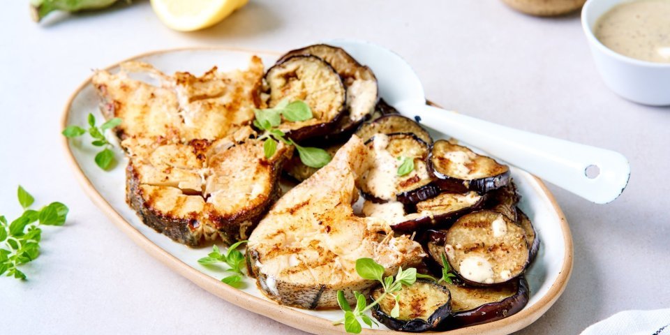 Een groot ovaal bord staat op tafel met de gebakken vismoten erop, samen met de gebakken aubergineschijfjes. De mosterpot van Tierenteyn staat er langs, samen met het gemaakt mosterdsausje. Het gerechtje werd afgewerkt met verse oreganoblaadjes. 