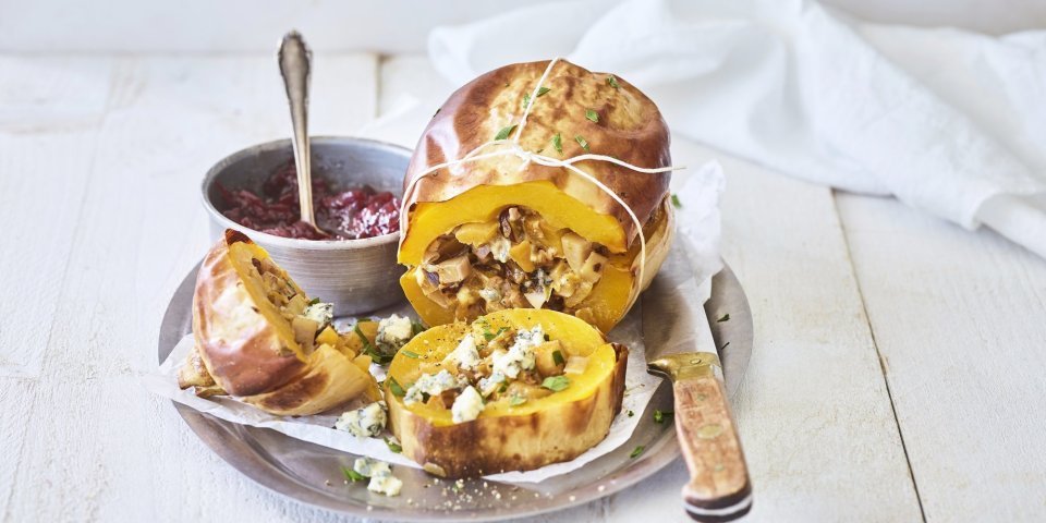 Een butternut-pompoen ligt op een schaal van inox. Hij is mooi opgevuld met een mengsel van krieltjes, preistukjes en blauweschimmelkaas. Wij combineren hem met veenbessencompote om een zoete smaak toe te voegen. 