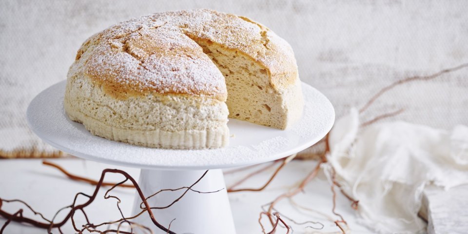 Een Japanse cheesecake, ook wel cheescakesoufflé genoemd, staat op een taartstandaard. Er is al 1 stukje aangesneden om meteen te smullen. 