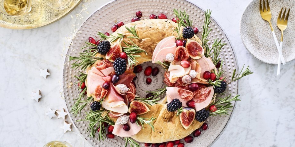 Een echte Kerstkrans om op te eten. De krans is gemaakt van een Turks brood die belegd werd met verschillende vleesjes, fruit en rozemarijn. Hij staat op de feesttafel en enkele zilveren sterren liggen er langs vergezeld met enkele aperitiefjes. 