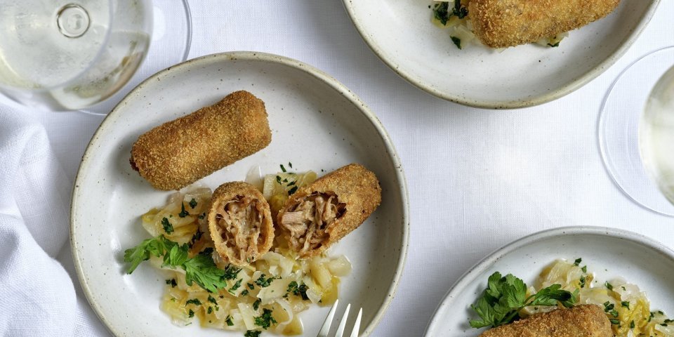 Meerdere kroketten liggen op kleine bleke bordjes. Ze worden geserveerd met huisgemaakte chutney van witloof. 