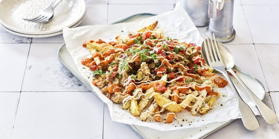 Op het aanrecht ligt een serveerschaal met een wit bakpapiertje op. Hierop liggen geroosterde aardappel, zoete aardappel en knolselder. Hierop strooien we paprika, gehakt en een sausje. Er staan bordjes langs om op te scheppen en aan te vallen. 