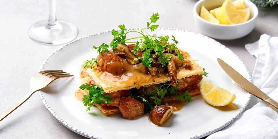 Een feestelijke kalfsfricassee staat op tafel, de ster van het menu. De fricassee ligt tussen twee knapperige vellen bladerdeeg met verse kervel en een partje citroen. 