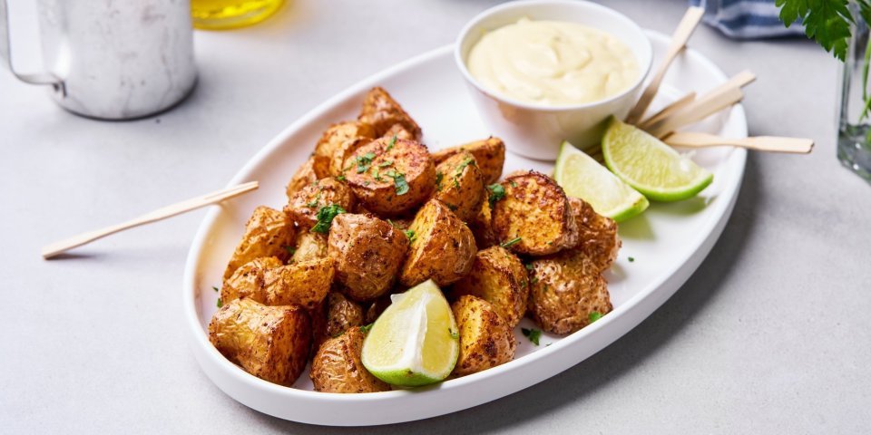 In een ovaal wit bord liggen de stukjes aardappel goudkrokant gebakken uit de airfryer. Er staat een dipsausje bij met enkele partjes limoen. We gebruiken houten vorkprikkertjes om de aardappel op te prikken en te dippen in het sausje. 