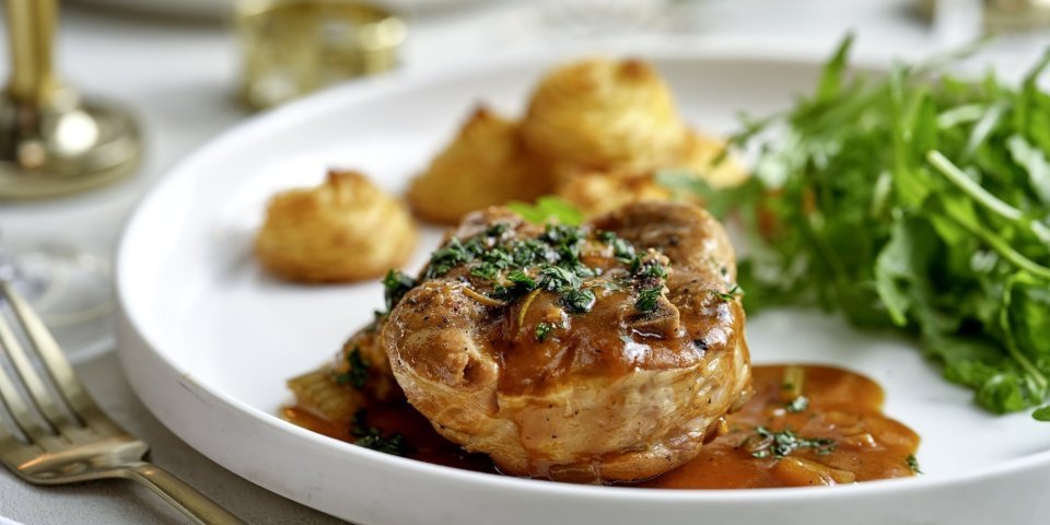 Het hoofdgerecht is geserveerd op een wit groot bord. Ieder krijgt een portie schenkel, pommes duchesse en frisse rucolasla. 