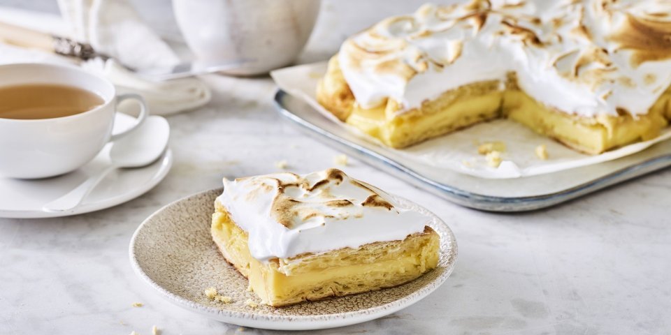 Croissanttaart staat aangesneden op tafel, thee is opgediend en bordjes staan klaar. De meringue is mooi gekleurd door de brulébrander. 