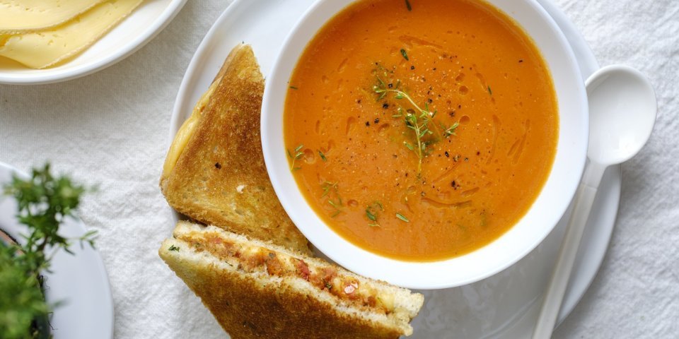 Een heerlijke kom soep staat klaar op tafel in een wit kommetje. Wij serveren hem met een toast van kaas en tomaatjes. Een heerlijke en voedzame lunch.