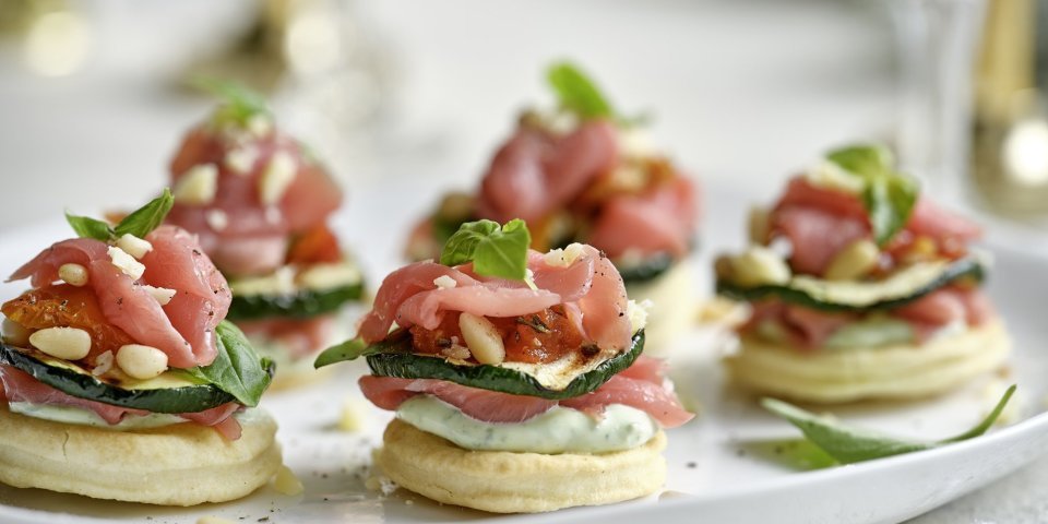 Feestelijke hapjes die de show stelen! Deze torentjes van kruimeldeeg, carpaccio en Belgische ricotta is een schot in de roos voor tijdens de feestdagen. Onderaan ligt een koekje van kruimeldeeg, hierop de ricotta met basilicum, rundvlees, gegrilde courgette en opnieuw rundvlees. Afwerken deden we met pijnboompitten en een extra blaadje basilicum.