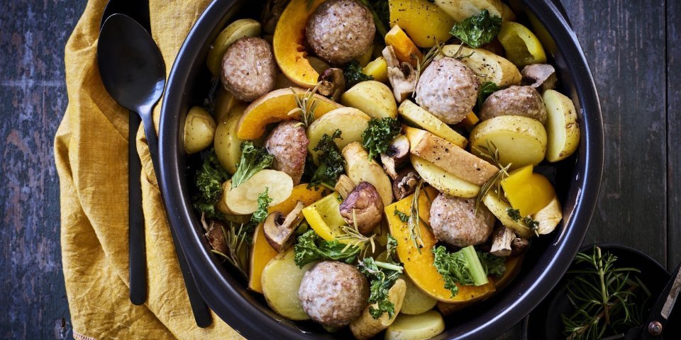 Een heerlijke kleurrijke traybake boordevol herfsttoppers. In een zwarte ronde ovenschotel werd een traybake klaargemaakt met aardappelblokjes, stukjes pompoen, boerenkool en gehaktballetjes. 