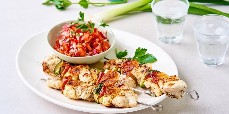 Enkele gegrilde brochettes liggen op een serveerschaal samen met een potje tomatensalsa. De salsa zorgt voor een mooie rode kleur bij de zeeduivelspiesjes.