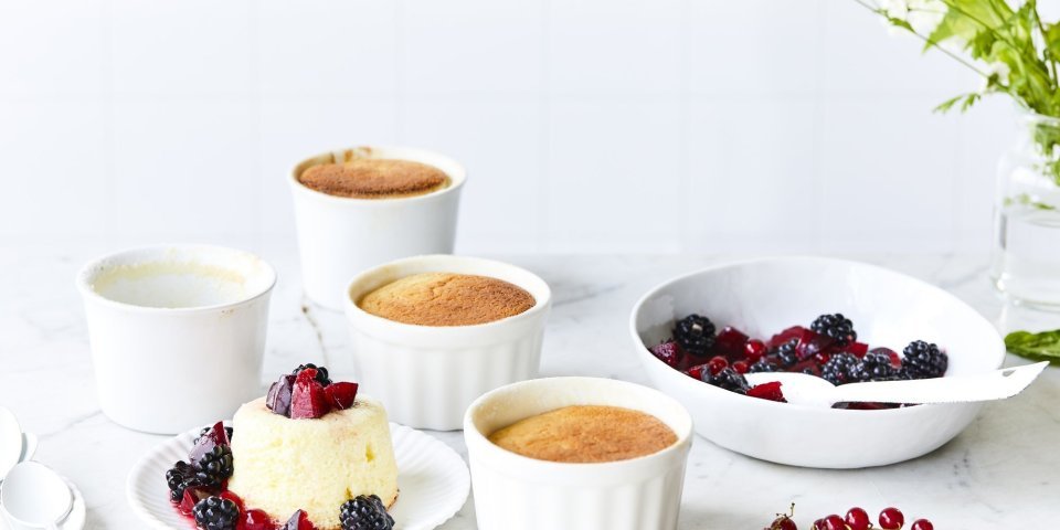 Er staan 4 soufflés op tafel, waarvan al eentje uit zijn ovenpotje. Het rood fruit ligt er langs, denk maar aan aardbeien, bessen en pruimen.