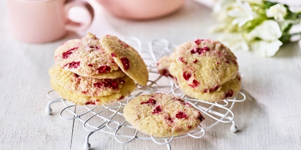 Op een kleine taartrooster liggen enkele koekjes te drogen. De koekjes hebben rode vlekjes van de framboosjes. Er staat een theepot langs met al een uitgeschonken thee in bijpassende roze tas. 