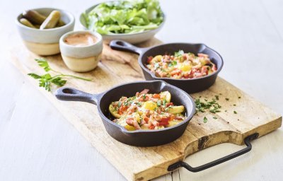 Twee gourmetpannetjes staan te sieren op een houten snijplank. Als bijgerechtjes hebben we een groene salade, opgelegde augurkjes en een cocktailsausje.